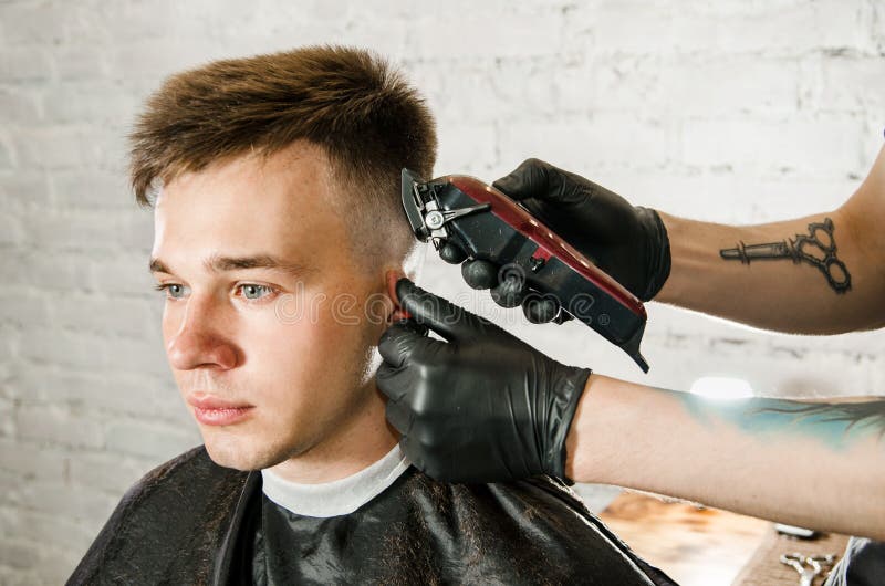 Friseurhand in den Handschuhen schnitt Haar und rasiert jungen Mann auf einem Backsteinmauerhintergrund Nahes hohes Portr?t eines