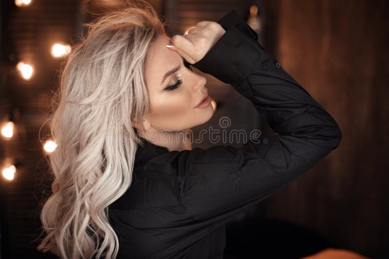 Frisyr Härlig blond kvinnastående som poserar i svart skjorta Trendig blond flickamodell över mörk bakgrund för bokehljus arkivfoto
