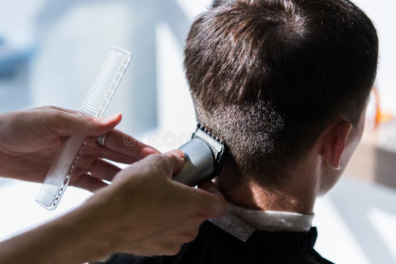 Frisören jämnar en frisyr med hjälpen av en rakapparat och en hårkam i en frisersalongnärbild royaltyfri foto Frisören jämnar en frisyr med hjälpen av en rakapparat och en hårkam i en frisersalongnärbild royaltyfri foto