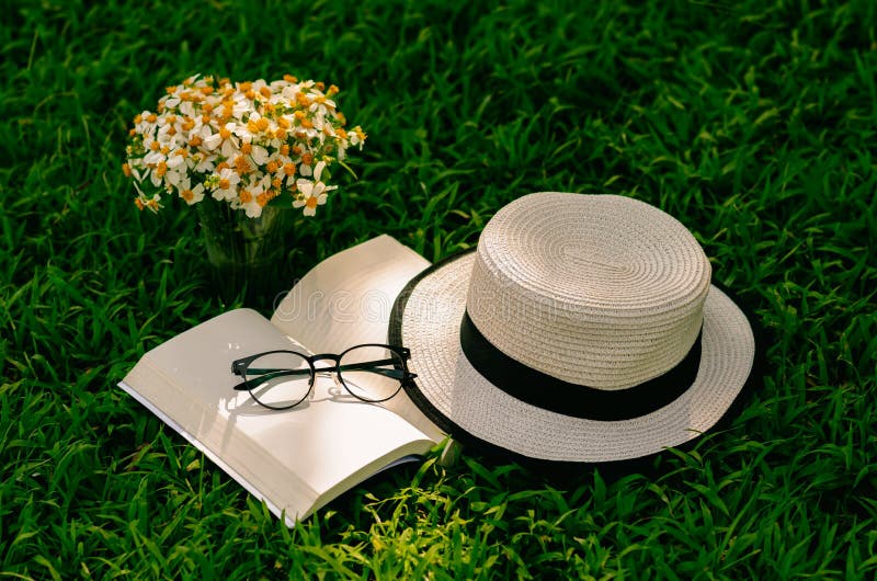 Leisure in the garden with book, straw hat, and flowers on the lawn. Leisure in the garden with book, straw hat, and flowers on the lawn.