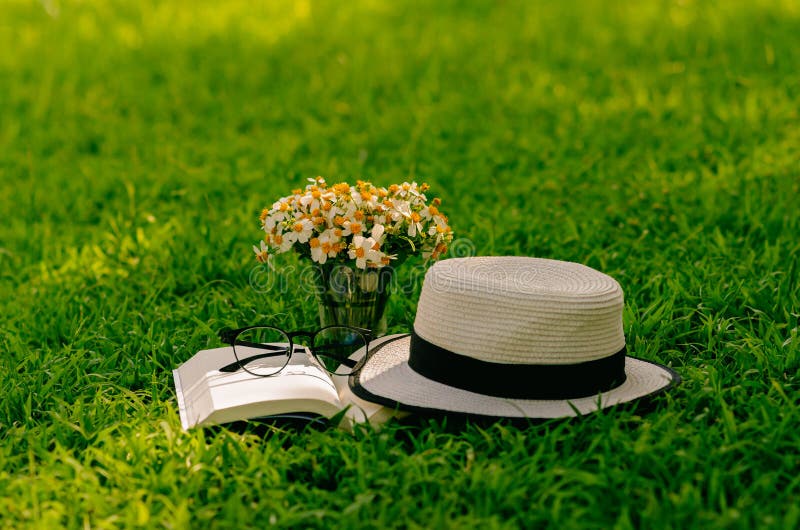 Leisure in the garden with book, straw hat, and flowers on the lawn. Leisure in the garden with book, straw hat, and flowers on the lawn