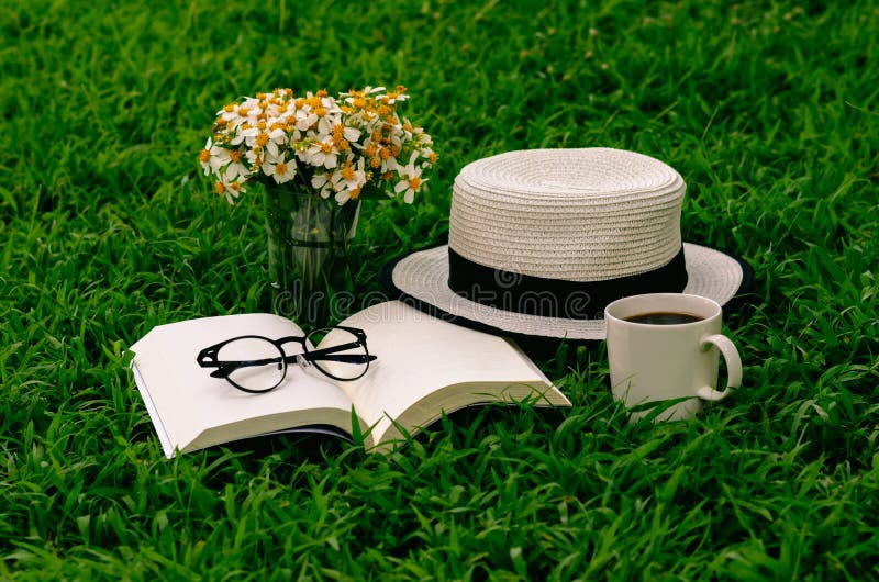 Leisure in morning at garden with coffee, book , hat and flowers on the lawn. Leisure in morning at garden with coffee, book , hat and flowers on the lawn.