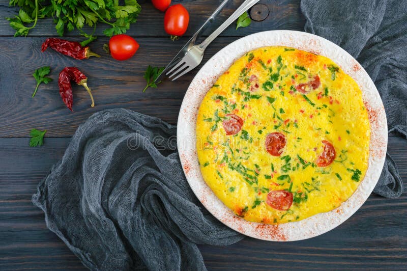 Frittata Omeleta italiana com queijo, verdes e tomates em uma placa branca em um fundo de madeira imagem de stock royalty free Frittata Omeleta italiana com queijo, verdes e tomates em uma placa branca em um fundo de madeira imagem de stock royalty free