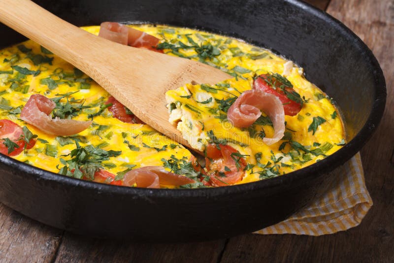 Frittata with tomato, ham and herbs in the pan with a spatula