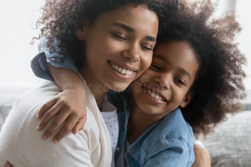 Frohe Afroamerikanermädchen, das ihre friedliche Mutter umfasst lizenzfreies stockbild