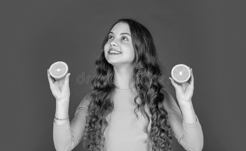 Frohe Teenager halten orangefarbene Früchte auf violettem Hintergrund lizenzfreie stockbilder