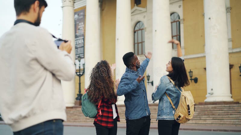 Frohe Touristenmänner und -frauen werfen für Kamera mit schönem Gebäude im Hintergrund lachend und springend während auf