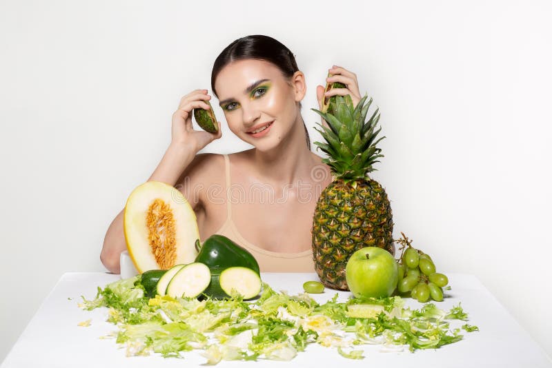Frohes sch?nes M?dchen mit dem hellen Kunstmake-uphalten schnitt frische Avocado in der Hand nahe Gesicht, Fr?chte in der Front G stockfotos Frohes sch?nes M?dchen mit dem hellen Kunstmake-uphalten schnitt frische Avocado in der Hand nahe Gesicht, Fr?chte in der Front G stockfotos