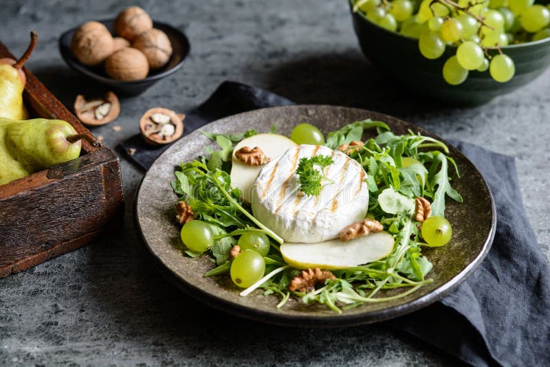 Fromage grillé de camembert avec l'arugula frais, les raisins verts, les poires et la noix image stock Fromage grillé de camembert avec l'arugula frais, les raisins verts, les poires et la noix image stock