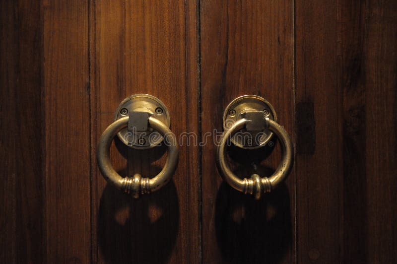 A photo taken on the front facing view of a wooden double doors with small knockers. A photo taken on the front facing view of a wooden double doors with small knockers.