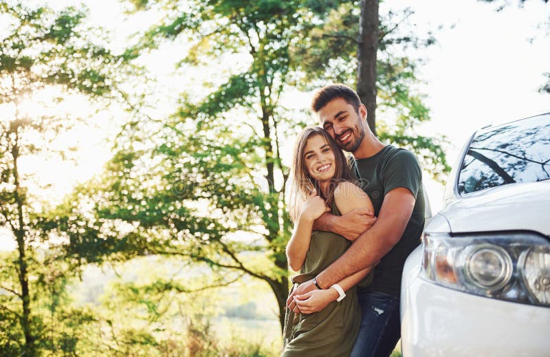 Front part of white car. Beautiful young couple have a good time in the forest at daytime