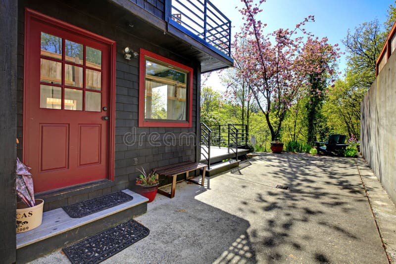 Front red door of black wood house with garden view.