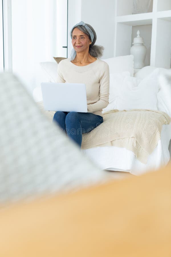 Woman Sitting On A Couch In A White Room While Using A White Laptop