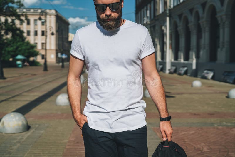 Front View Der junge bärtige tausendjährige Mann, der im weißen T-Shirt und in der Sonnenbrille gekleidet wird, ist Stände auf St lizenzfreie stockfotografie