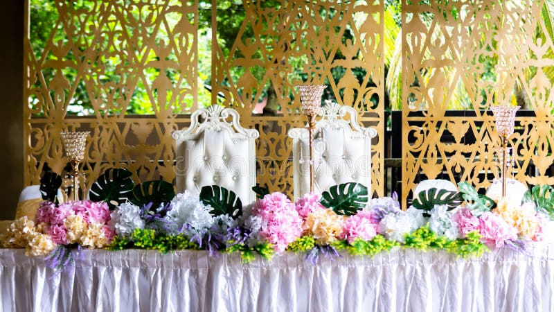 The front view of the dining table of the weeding ceremony during lunch. The King and Queen of the day. Floral, elegant and minimalist design. Bright and white concept, wedding, event, food, couple, flower, beautiful, light, background, chair, garden, interior, catering, elegance, shiny, malaysian, bridal, muslim, traditional, arrangement, glass, pretty, ribbon, luxury, detail, romance, beauty, bouquet, romantic, love, marriage, decoration, celebration, place, grand, set, majestic, bride, groom