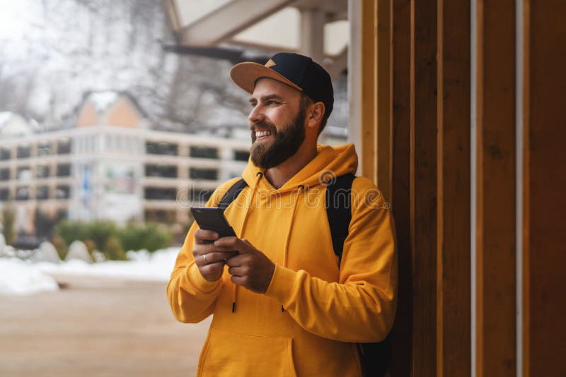 Vista frontal. Turista do sexo masculino com barba, vestindo um casaco de capuz amarelo e boné com uma mochila preta, está ao ar l fotos de stock royalty free