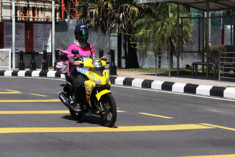 Frontal view of a Malay female Foodpanda delivery rider out on the streets of Ipoh, Malaysia. The woman`s face is not visible being shielded by the visor mounted on the helmet. Frontal view of a Malay female Foodpanda delivery rider out on the streets of Ipoh, Malaysia. The woman`s face is not visible being shielded by the visor mounted on the helmet