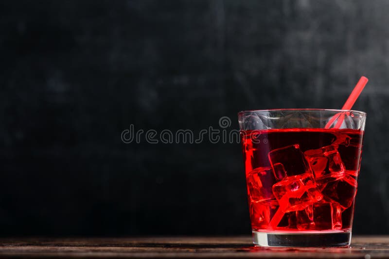 Front view of glass of red cocktail with ice cubes on dark wooden table, copyspace for text