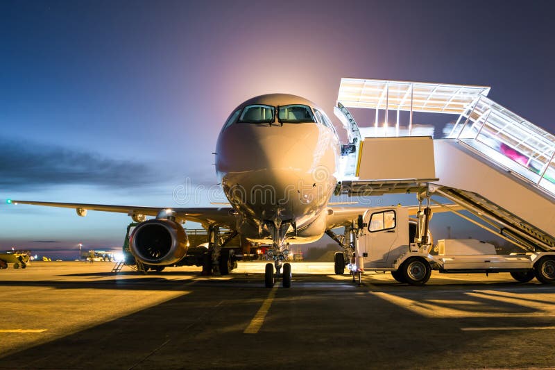 Front view ground handling of white passenger airplane with a boarding steps at the night airport apron stock image Front view ground handling of white passenger airplane with a boarding steps at the night airport apron stock image
