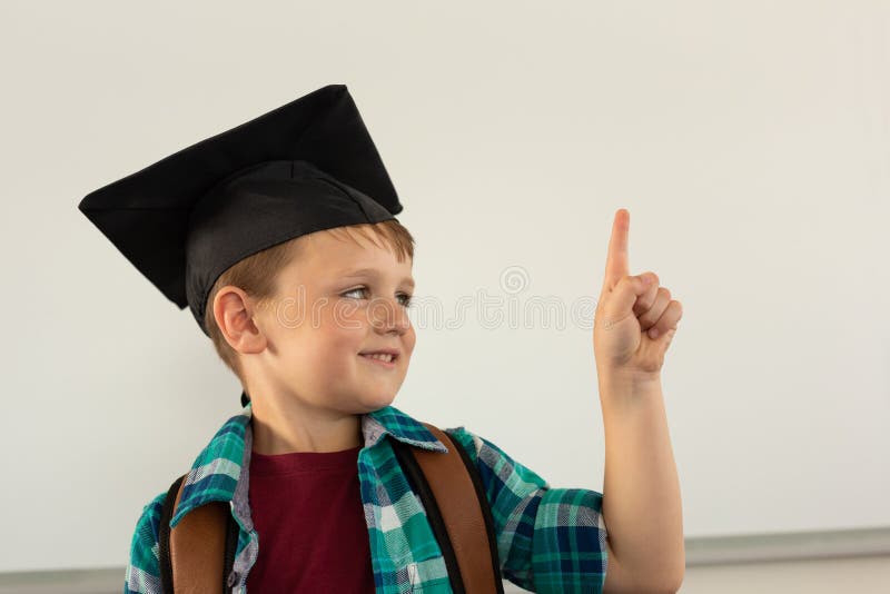 Happy boy in graduation cap pointing his finger in a classroom royalty free stock image Happy boy in graduation cap pointing his finger in a classroom royalty free stock image