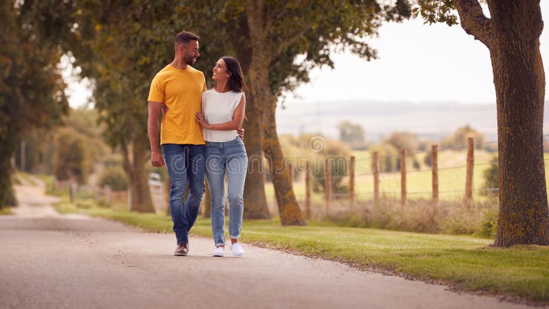 Front View Of Loving Couple Hugging As They Walk Along Track Through Countryside stock photo