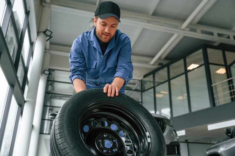 Front View, Moving the Tire. Man in Blue Uniform is Working in the Car