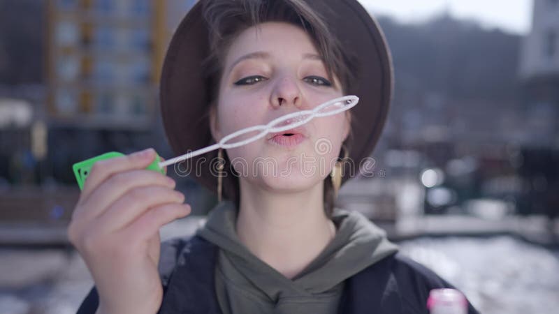 Front view portrait of relaxed beautiful woman blowing soap bubbles in slow motion and looking at camera. Close-up of