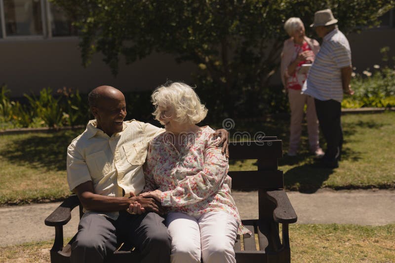 Front view of senior couple holding hands and sitting on bench in garden royalty free stock photo Front view of senior couple holding hands and sitting on bench in garden royalty free stock photo