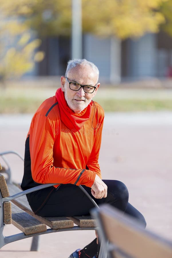 Front view of a senior man in sports clothes sitting in a bench at park while smiling and looking camera in a sunny day stock images Front view of a senior man in sports clothes sitting in a bench at park while smiling and looking camera in a sunny day stock images