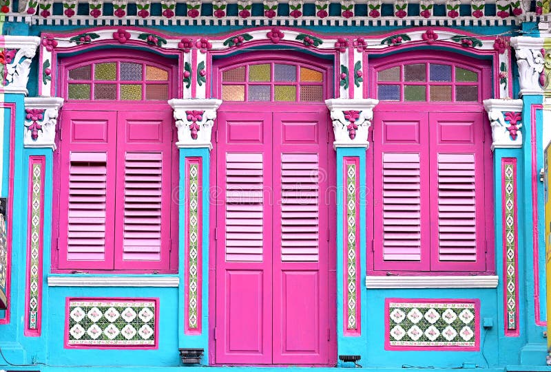 Exterior of blue Singapore Straits Chinese Peranakan shophouse with arched windows, pink wooden louvered shutters & ornate columns