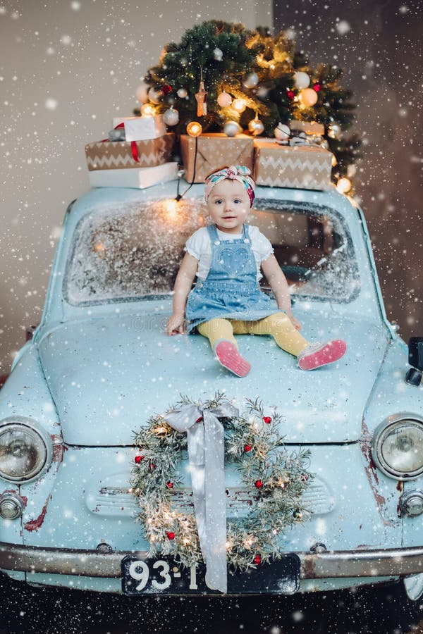 Front view of sweet and fashionable little cute girl sitting on blue retro car decorated for Christmas. stock photography Front view of sweet and fashionable little cute girl sitting on blue retro car decorated for Christmas. stock photography
