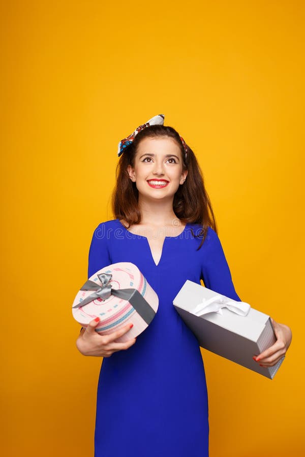 Cheerful girl in blue dress holding heap of presents, looking up, on yellow background. Copy space. stock photography Cheerful girl in blue dress holding heap of presents, looking up, on yellow background. Copy space. stock photography