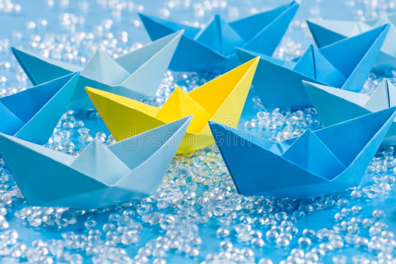 A frota do papel azul do origâmi envia na água azul como o fundo que cerca amarelo imagem de stock royalty free A frota do papel azul do origâmi envia na água azul como o fundo que cerca amarelo imagem de stock royalty free