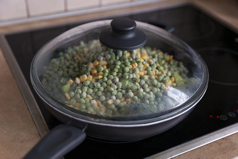 Frozen Mix of Vegetables in a Frying Pan on the Stove. Closeup Stock