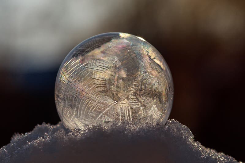 Frozen soap bubble with a beautiful pattern on the snow close-up on a blurry background. Frozen soap bubble with ice crystals at sunlight. Soap snowflake stock images, royalty-free photos and pictures