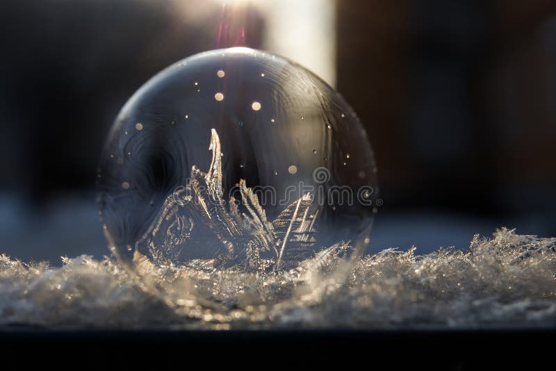 Frozen soap bubble with a beautiful pattern on the snow close-up on a blurry background. Frozen soap bubble with ice crystals at sunlight. Soap snowflake stock images, royalty-free photos and pictures