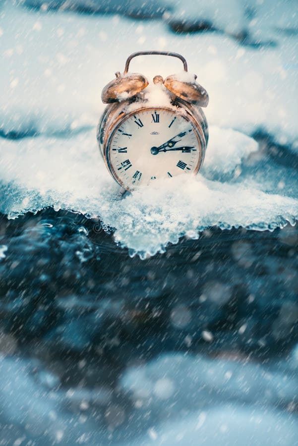 Frozen time. A clock on an ice next to the water. Extreme weather situation. Snow falling on a clock in a nature.