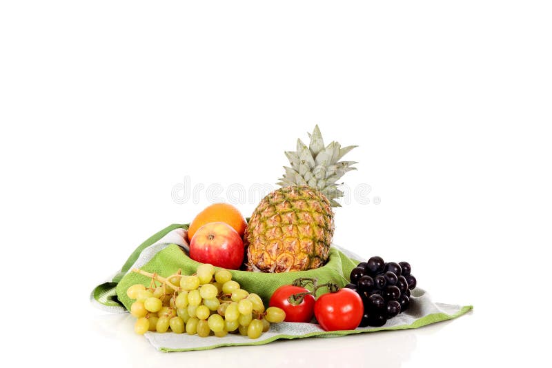 Fruit basket with oranges, apples, pineapple, tomatoes and grapes on towel. Reflective surface, studio, white background. Fruit basket with oranges, apples, pineapple, tomatoes and grapes on towel. Reflective surface, studio, white background.