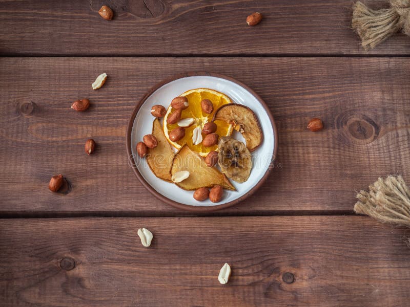Fruit chips without sugar and additives on a small plate and peanuts, the plate is on a wooden tray, for a healthy snack stock photography Fruit chips without sugar and additives on a small plate and peanuts, the plate is on a wooden tray, for a healthy snack stock photography