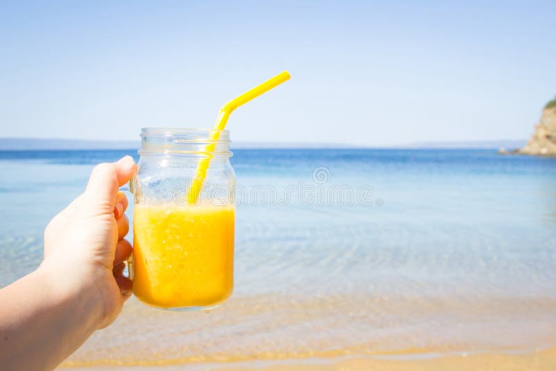 Fruit cocktail in woman hand against tropical beach. Summer refreshment. Travel and vacation concept. Copy space stock image Fruit cocktail in woman hand against tropical beach. Summer refreshment. Travel and vacation concept. Copy space stock image