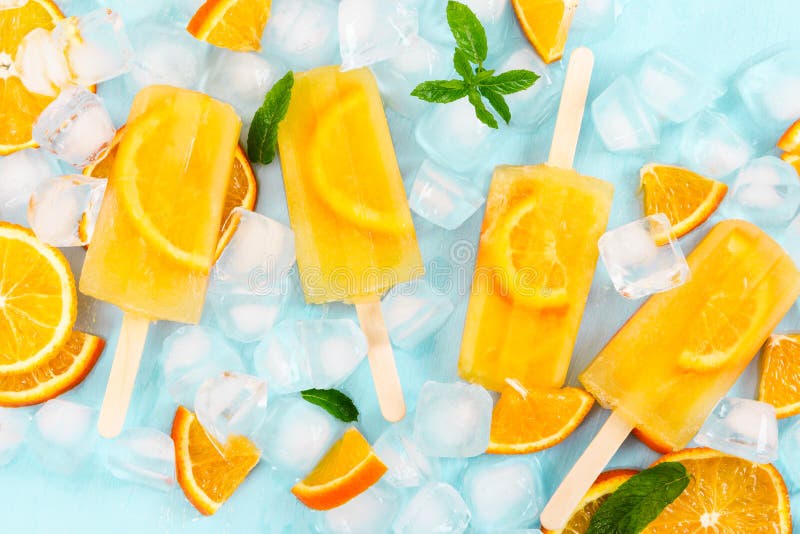 Fruit homemade popsicle with slices of orange and ice cubes on light blue background. Top view.