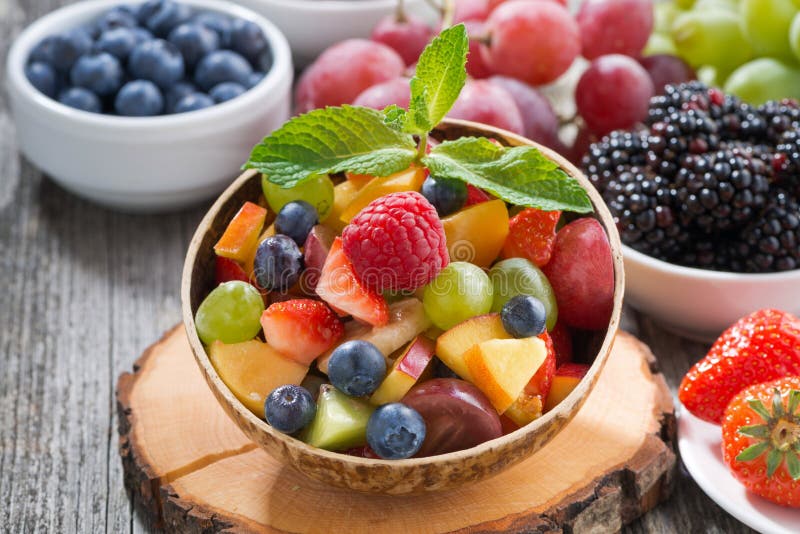 Fruit salad in a bamboo bowl and fresh berries, close-up