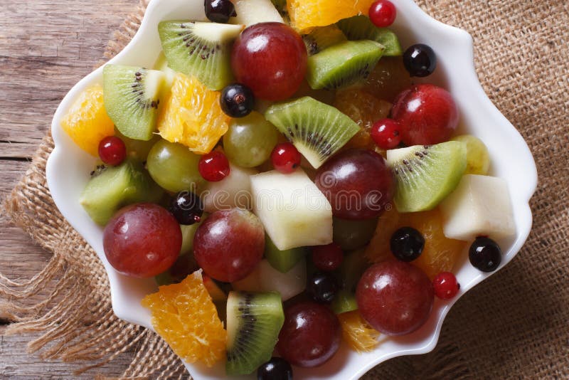 Fruit salad in white plate close-up horizontal top view, rustic