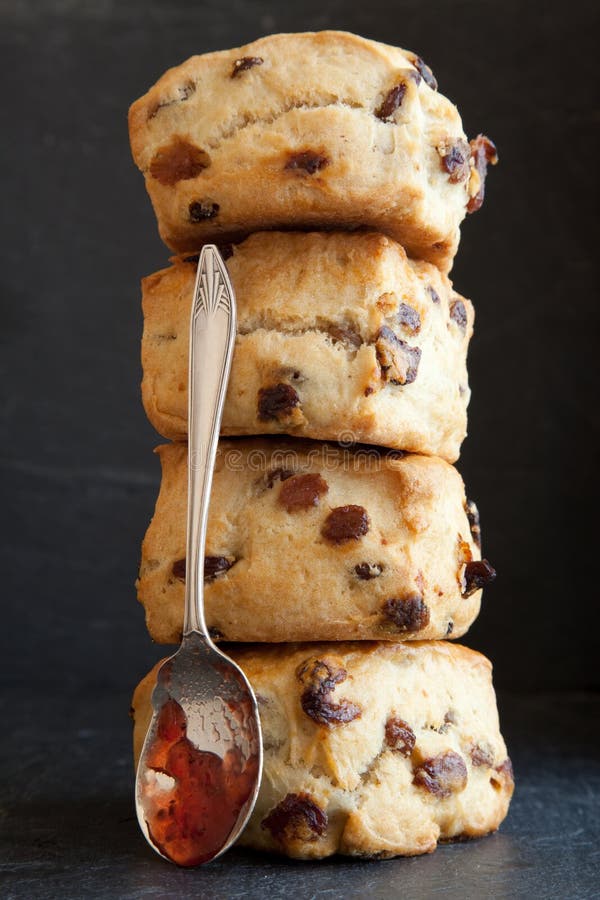 Four fruit scones stacked vertically with a silver spoon resting against the scones and jam running from the spoon. Four fruit scones stacked vertically with a silver spoon resting against the scones and jam running from the spoon