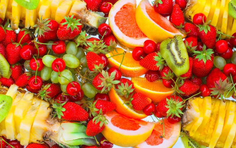 Fruit sliced oranges, banana, kiwi, cherries, grapefruit, strawberries, grapes and pineapple lying on a white plate