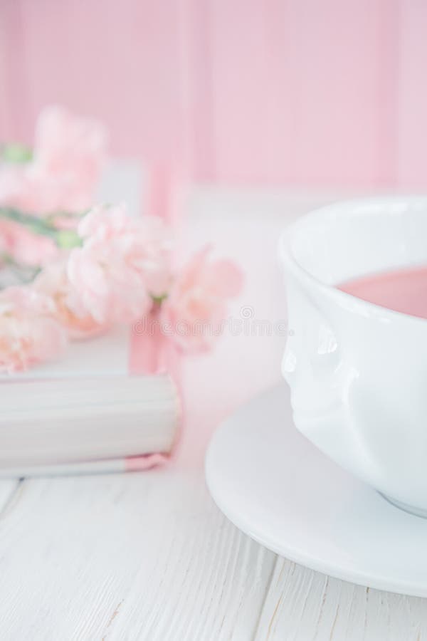 Fruit tea in white cup, book and pink carnation flowers on a white background. Free space