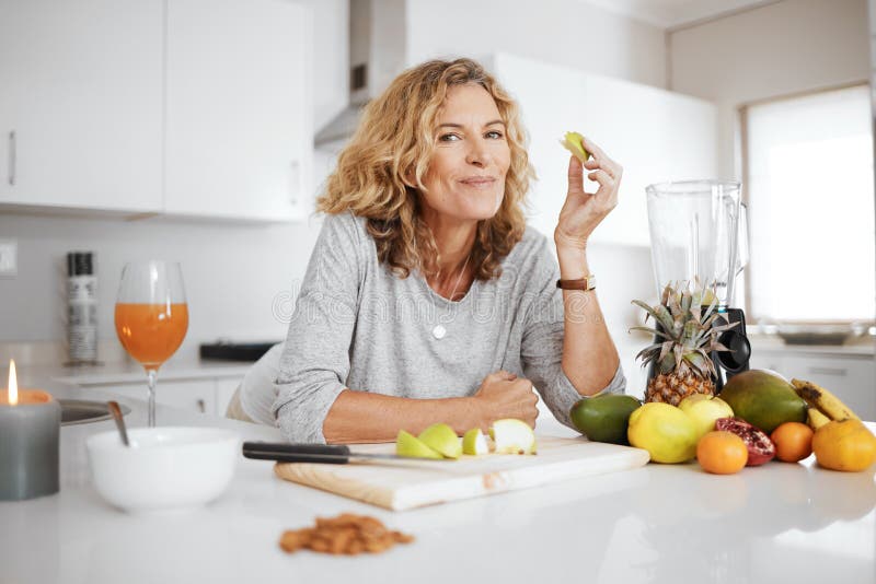 Fruits are natures candy. a woman preparing and eating fruit before making a smoothie.