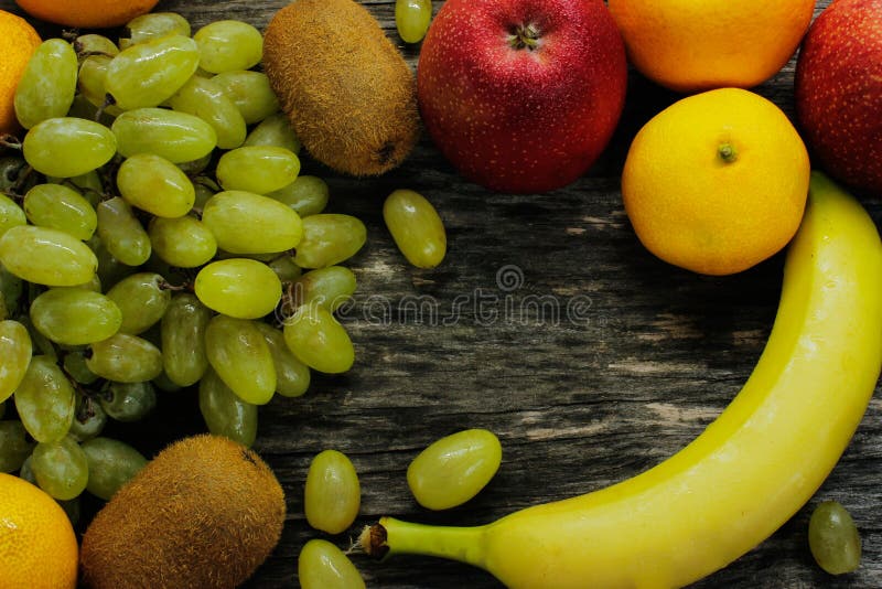 Fruitschotel van verse mandarins, kiwi, rode appelen en bananen, druiven, op grijze houten lijst stock fotografie Fruitschotel van verse mandarins, kiwi, rode appelen en bananen, druiven, op grijze houten lijst stock fotografie
