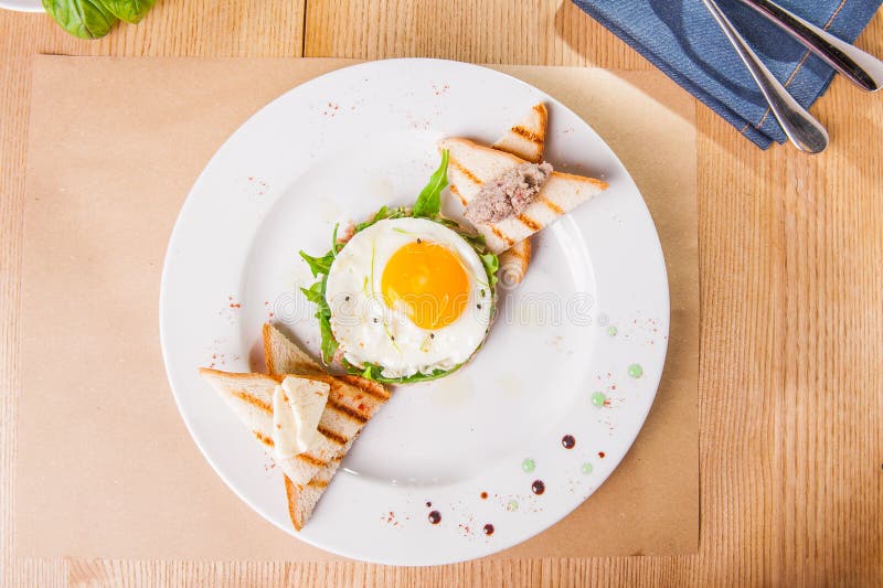 Frukost för bästa sikt med stekte ägg, rostade bröd och köttpate på den vita plattan på den tjänade som trätabellen Selektiv foku arkivbilder Frukost för bästa sikt med stekte ägg, rostade bröd och köttpate på den vita plattan på den tjänade som trätabellen Selektiv foku arkivbilder