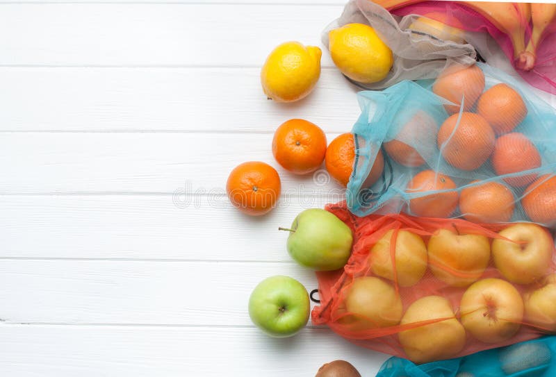 Frukter i eco-vänskapsmatch shoppingpåsar på vit träbakgrund med kopieringsutrymme arkivfoton